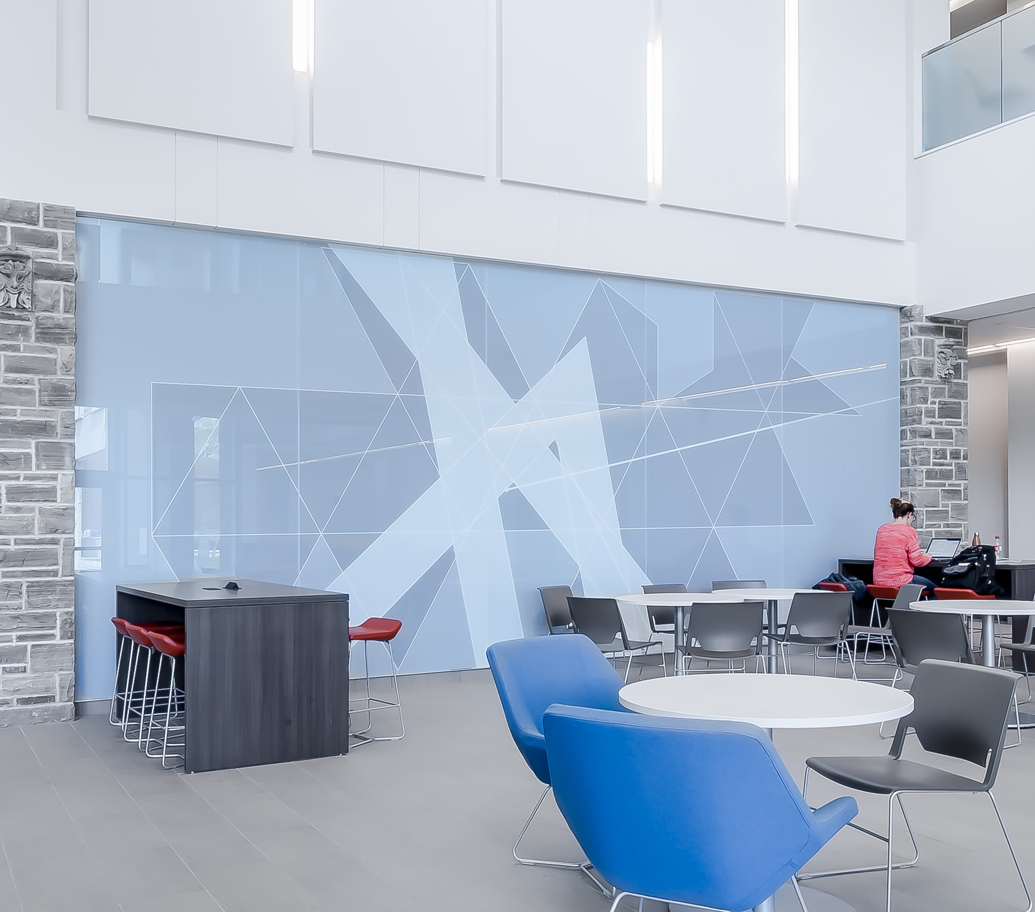 Clean open-concept lobby with geometric vinyl wrapped wall and with blue and grey chairs and white table featured in bottom right corner