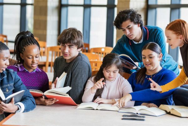 A group of students at a library table reading books and talking.