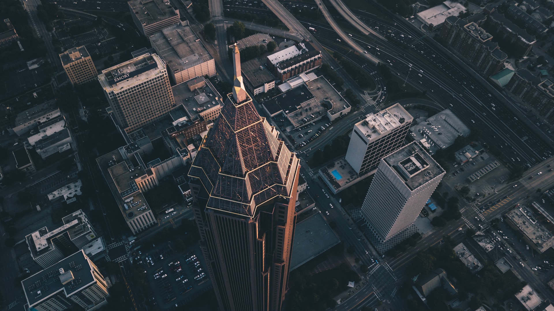 Looking out from the sky at an urban skyscraper surrounded by smaller buildings.